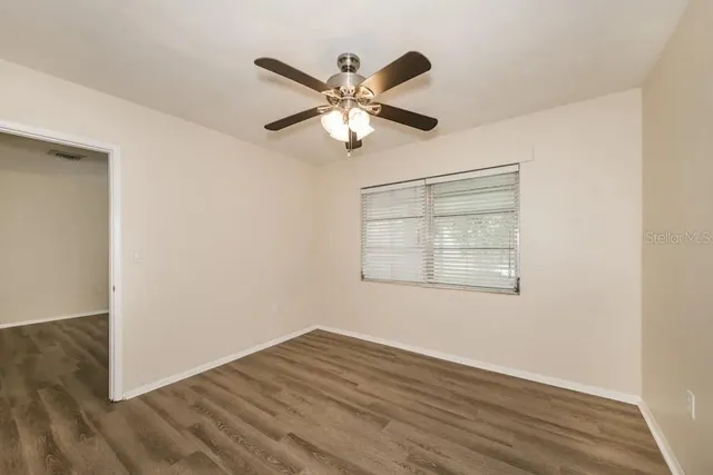 a view of an empty room with wooden floor and a ceiling fan