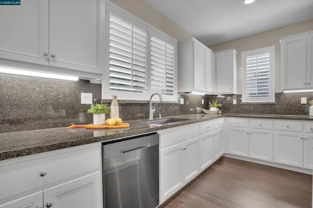 a kitchen with granite countertop stainless steel appliances white cabinets and a window