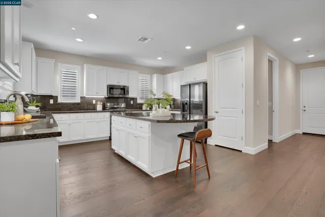 a kitchen with stainless steel appliances granite countertop a stove a sink a refrigerator and white cabinets