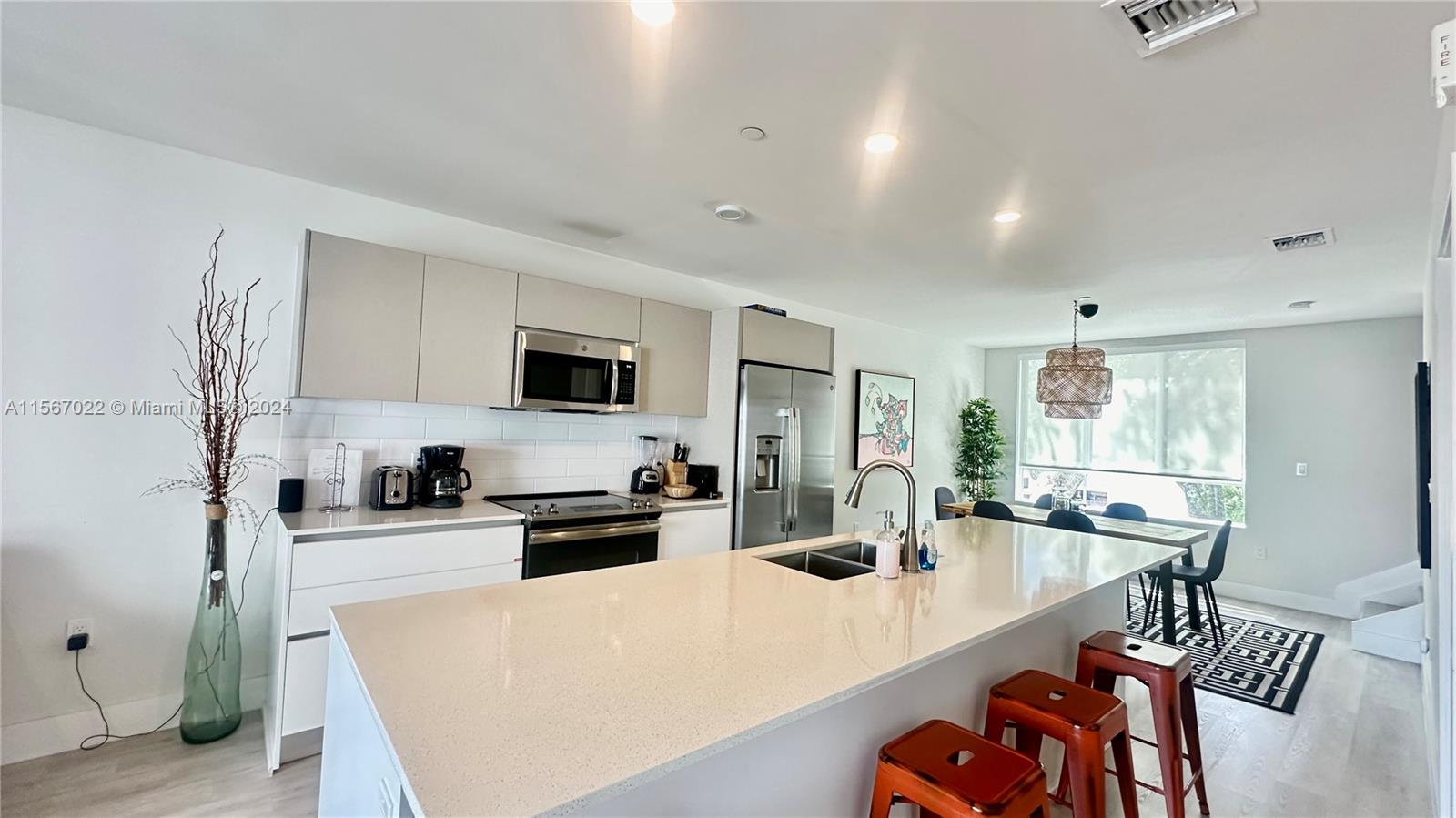 a kitchen with stainless steel appliances a sink a stove a refrigerator a dining table and chairs with wooden floor