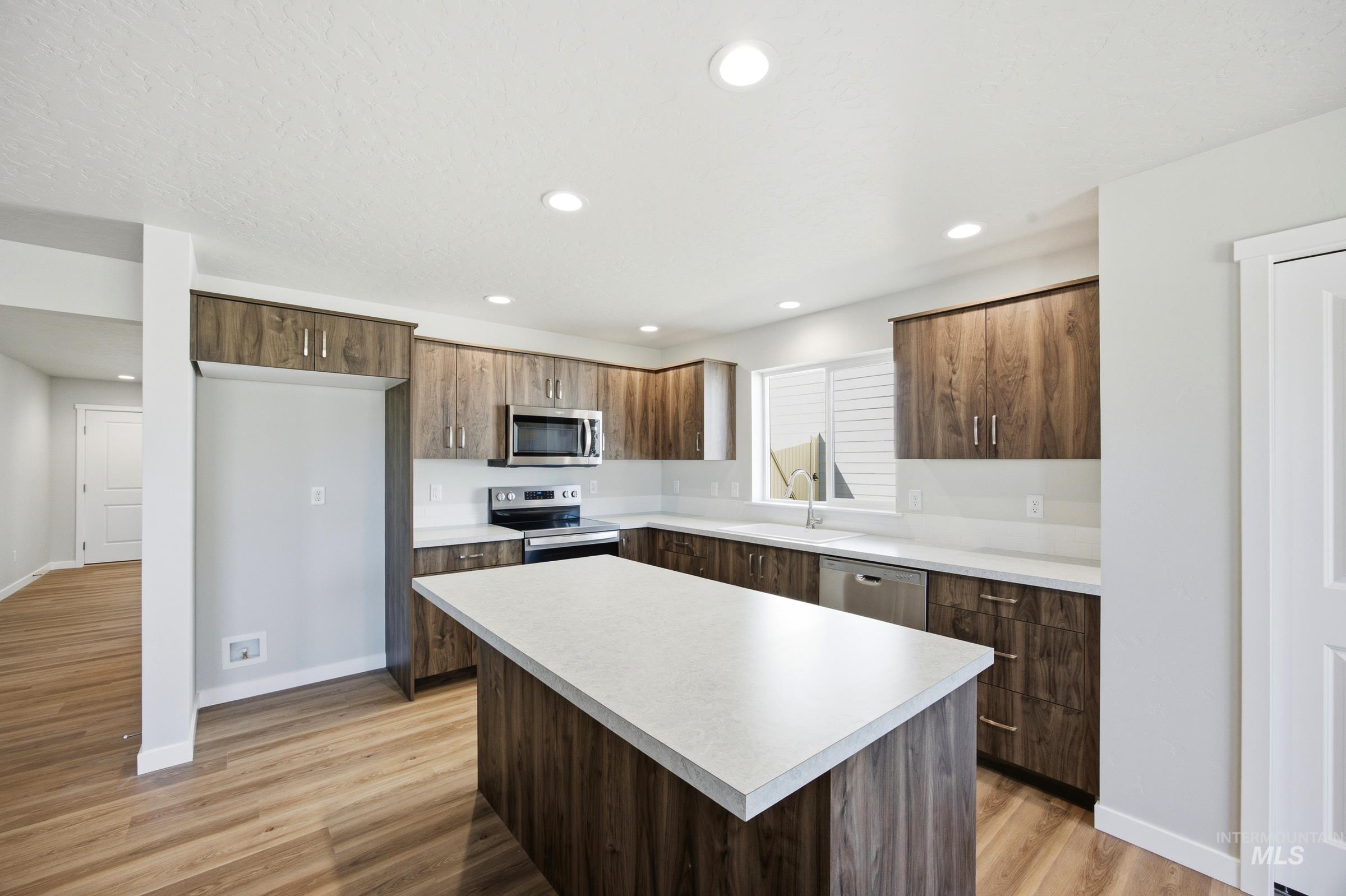 13333 Bank Street Caldwell, ID 83607 - Photo 10 of 29 Modern kitchen featuring wood-finish cabinetry, light-toned countertops, a central island, stainless steel appliances, and wood-finish flooring