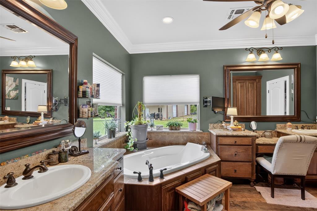 11868 Timber Ridge Drive Keithville, LA 71047 - Photo 16 of 37 Bathroom featuring a built-in corner soaking tub, dual vanities with integrated sinks, granite countertops, wood-finish cabinetry, and a dedicated vanity seating area