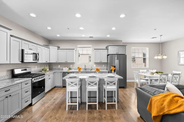 a kitchen with stainless steel appliances granite countertop a stove top oven a sink dishwasher a dining table and chairs with wooden floor