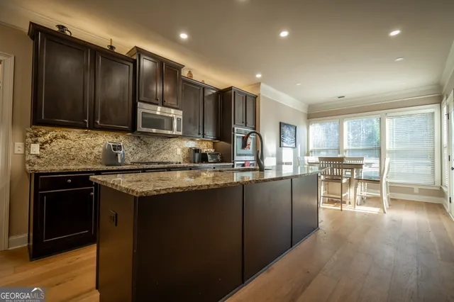 a kitchen with stainless steel appliances granite countertop wooden cabinets a refrigerator a sink a stove a microwave and wooden cabinets