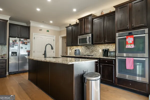 a kitchen with stainless steel appliances granite countertop a refrigerator a sink dishwasher and wooden cabinets with wooden floor