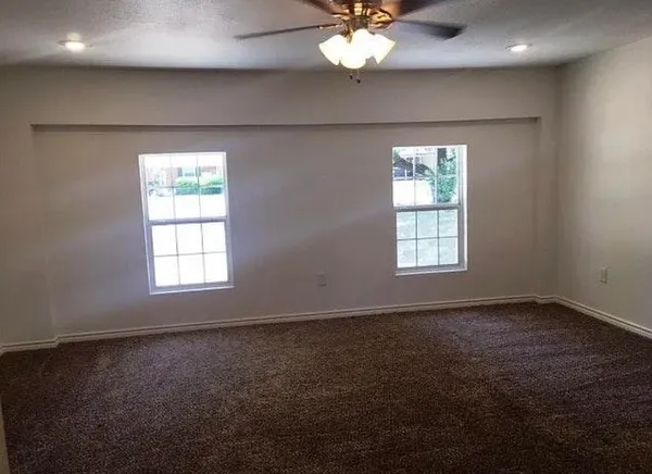 an empty room with a chandelier fan and windows