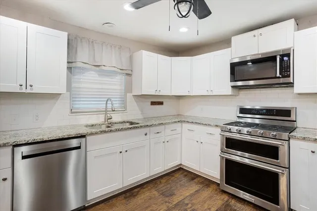 a kitchen with granite countertop a sink stainless steel appliances and white cabinets