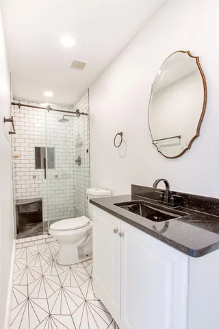 a bathroom with a granite countertop sink a mirror a toilet and a shower