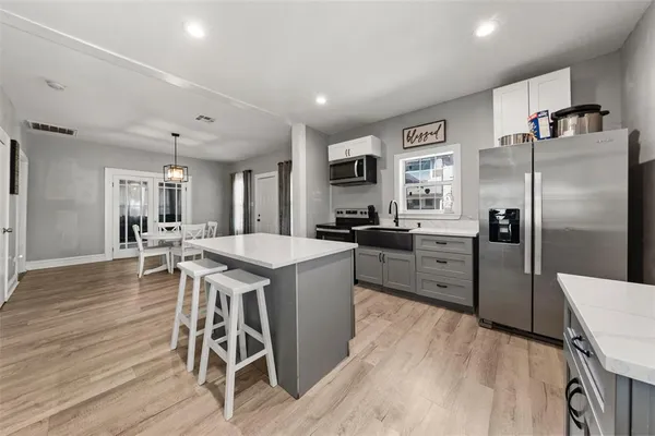 a kitchen with stainless steel appliances kitchen island granite countertop a refrigerator a stove a sink a dining table and chairs with wooden floor