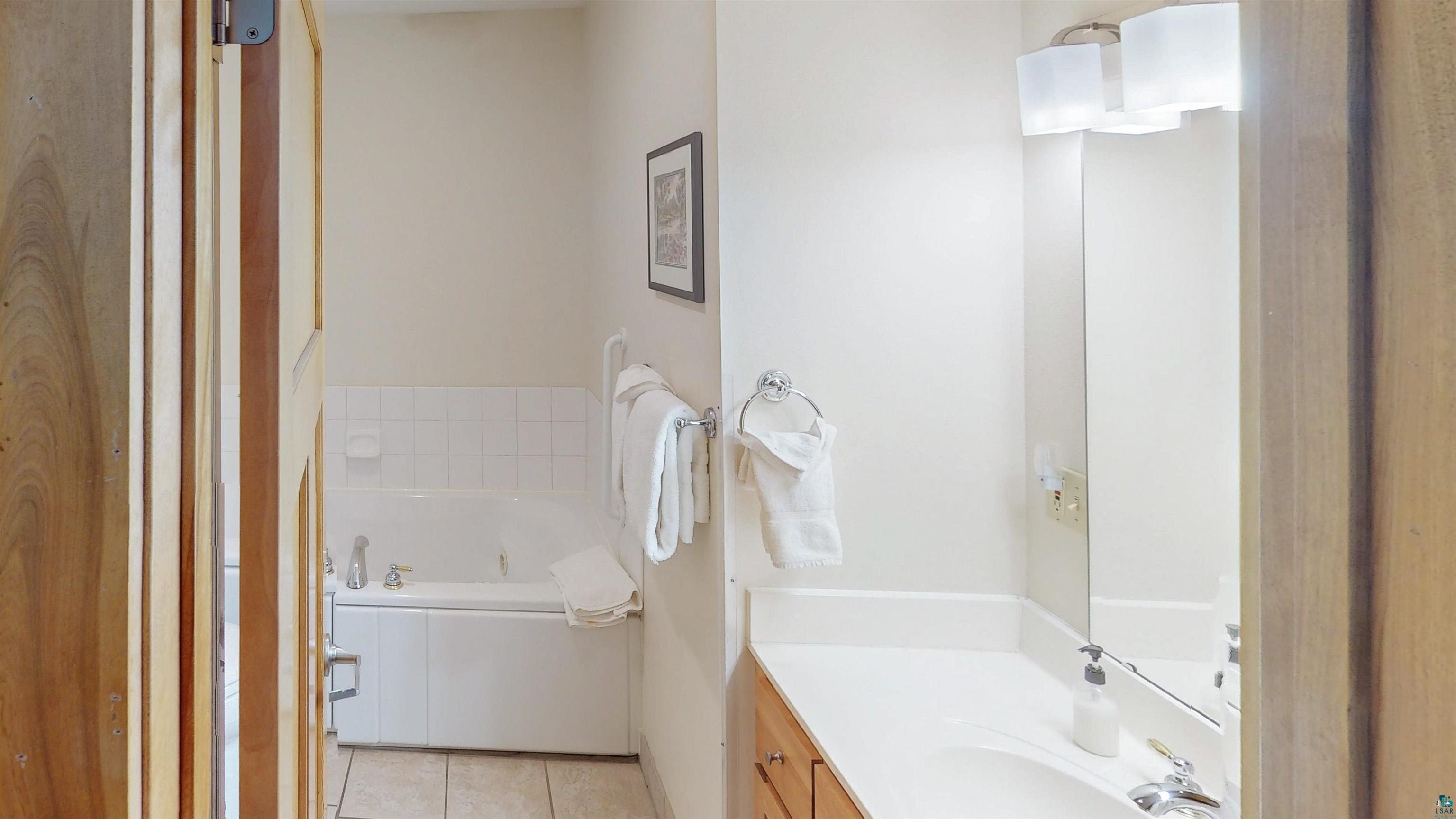 504-506 Poplar River Road, Unit 505 Lutsen, MN 55612 - Photo 16 of 39 Bathroom featuring a single vanity with wood cabinetry, a built-in bathtub with subway tile surround, and tile flooring