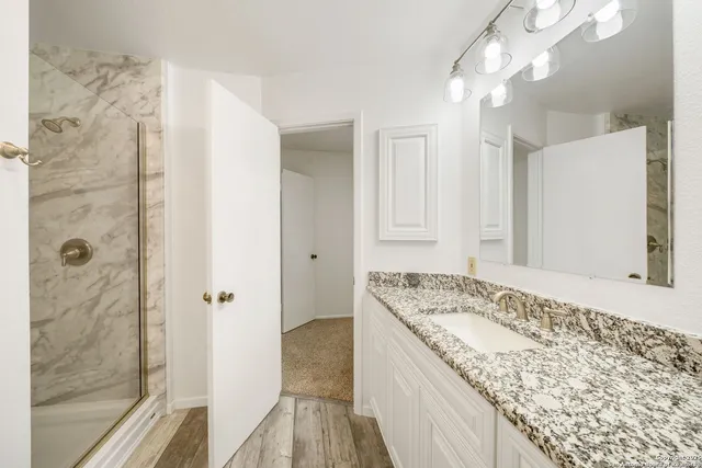a bathroom with a granite countertop sink a mirror and shower