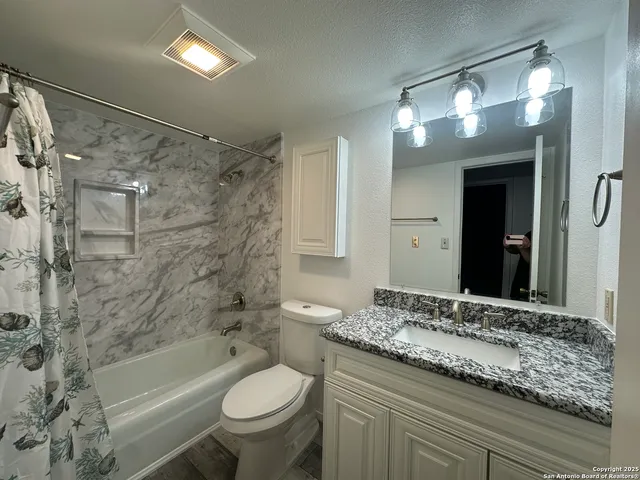 a bathroom with a granite countertop sink a toilet a mirror a bathtub and shower