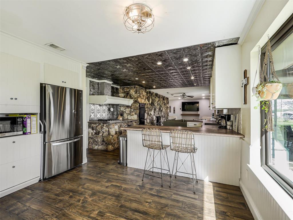 62 Sanders Road Whitesboro, TX 76273 - Photo 8 of 19 The kitchen features a functional breakfast bar with seating, flowing seamlessly into the home’s standout natural stone fireplace wall.