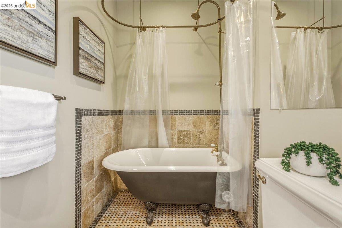 1631 La Vereda Road Berkeley, CA 94709 - Photo 17 of 42 Clawfoot bathtub with an overhead shower fixture, complemented by natural stone tile wainscoting and mosaic accents