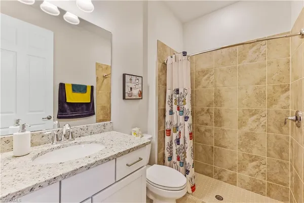 a bathroom with a granite countertop sink a toilet a mirror a vanity and shower