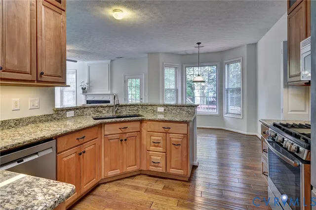 a large kitchen with granite countertop a stove a sink dishwasher and wooden cabinets with wooden floor