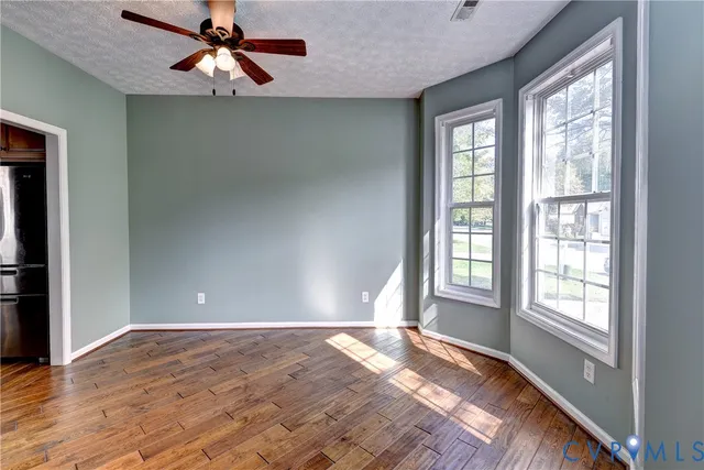 an empty room with wooden floor fan and windows