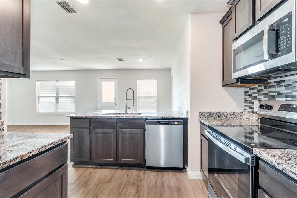 144 Barbwire Way Newark, TX 76071 - Photo 5 of 24 a kitchen with stainless steel appliances granite countertop a stove a sink dishwasher and microwave oven with wooden floor