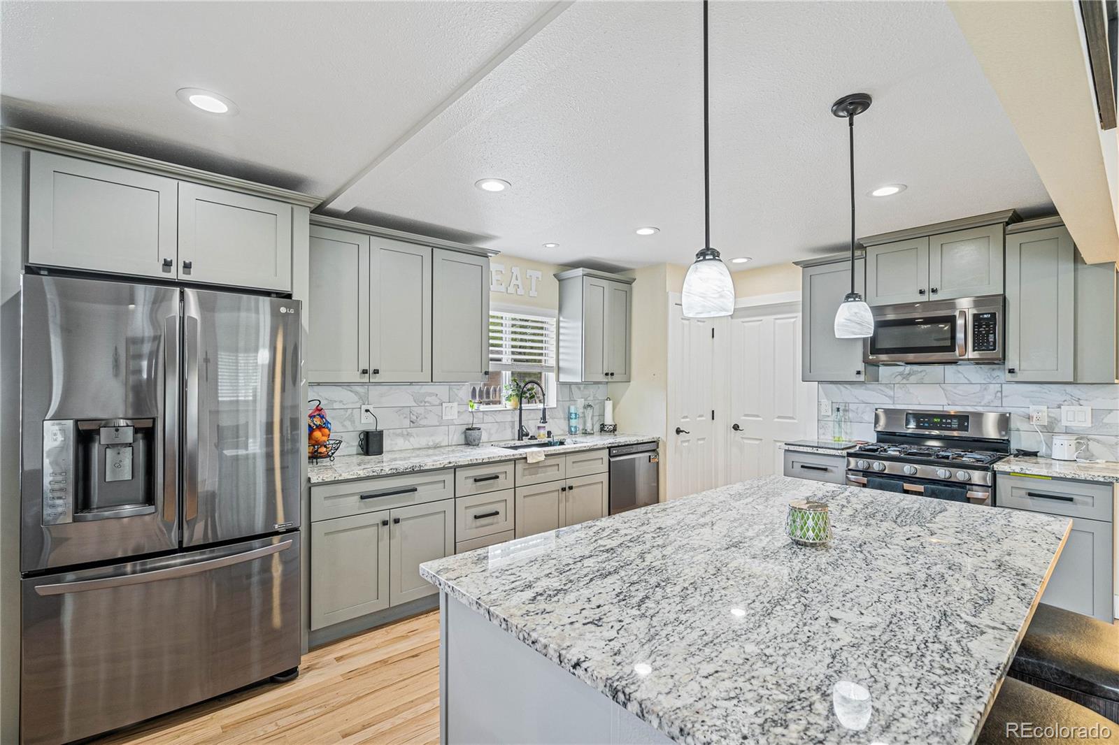 a kitchen with stainless steel appliances granite countertop a refrigerator a sink dishwasher a stove top oven a kitchen island and chairs with wooden floor