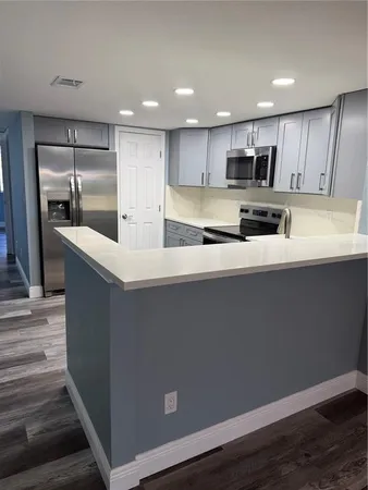 a large white kitchen with kitchen island a sink a stove a refrigerator and grey cabinets