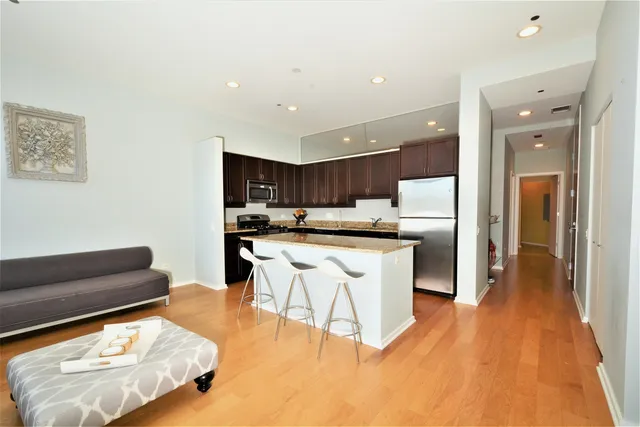 a kitchen with stainless steel appliances kitchen island granite countertop a refrigerator a sink a stove and white cabinets with wooden floor