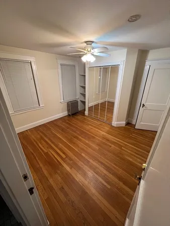 a view of an empty room with wooden floor and a ceiling fan