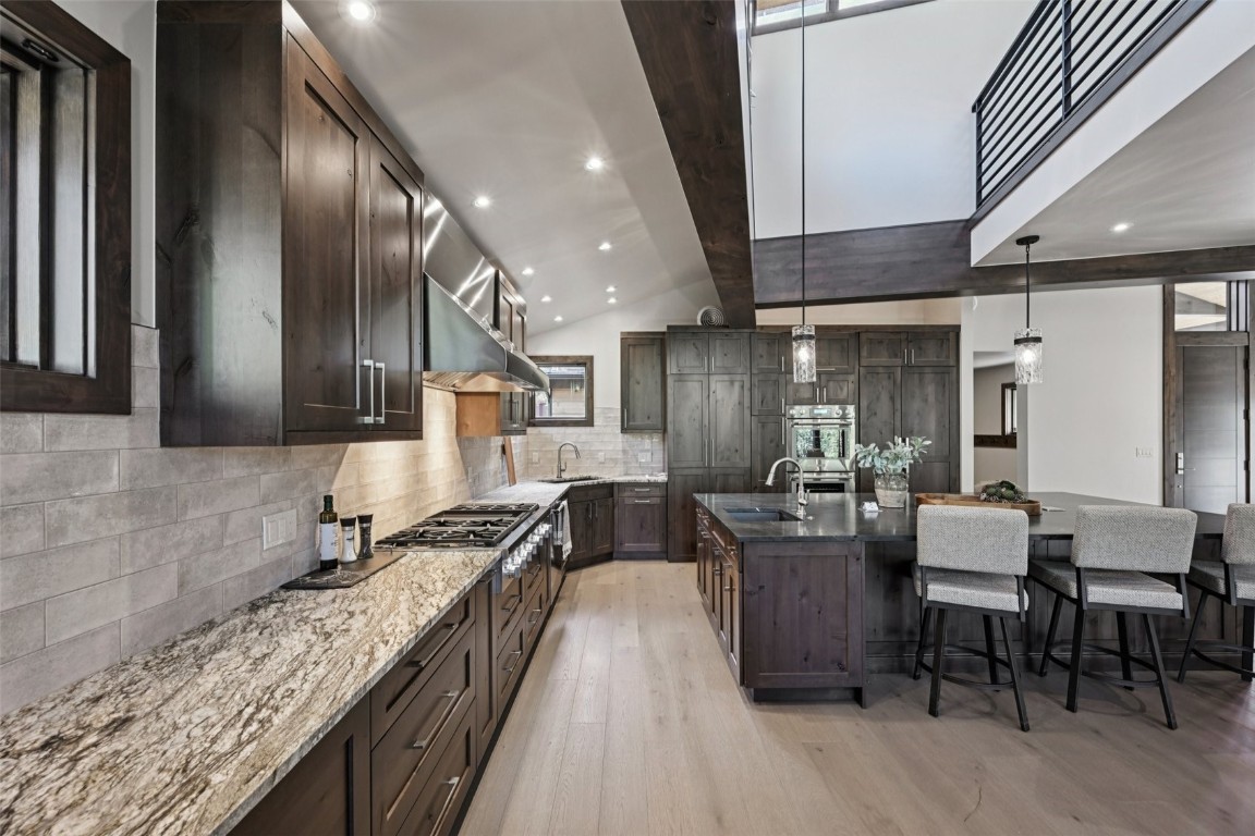 27 West Independence Road Keystone, CO 80435 - Photo 15 of 48 Kitchen with light wood finished floors, dark stone countertops, dark brown cabinets, a kitchen bar, and backsplash