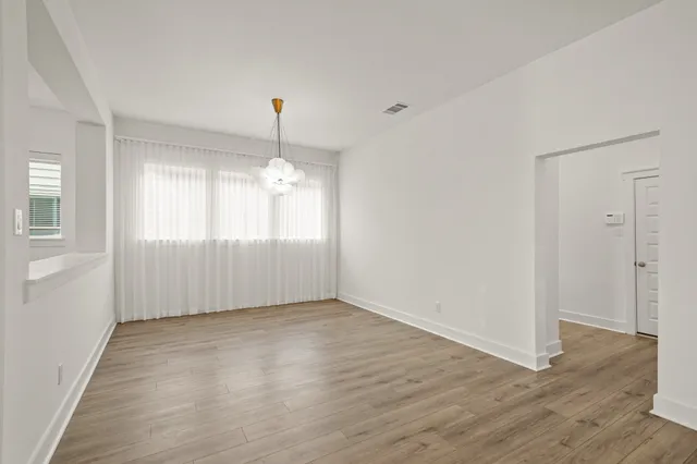 an empty room with wooden floor chandelier and windows