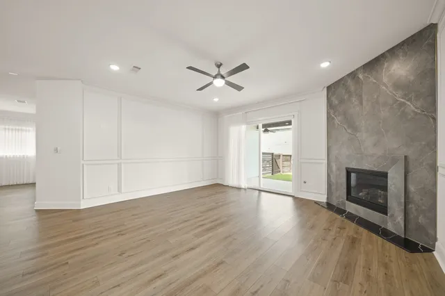 an empty room with wooden floor a ceiling fan a fireplace and windows