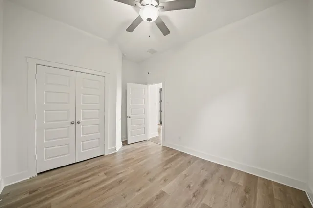 an empty room with wooden floor ceiling fan and windows