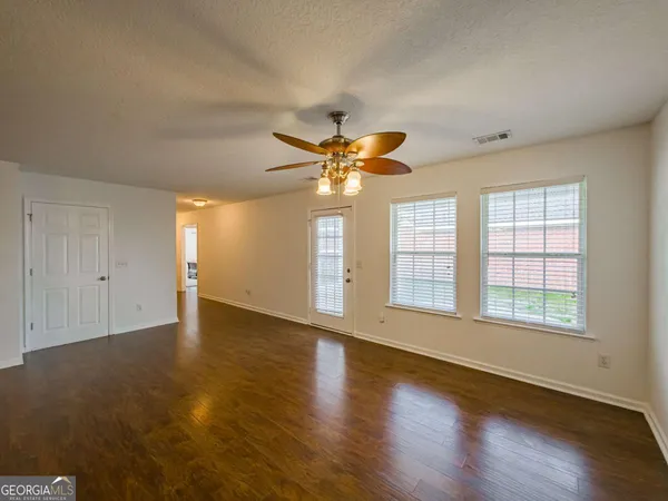 an empty room with wooden floor chandelier fan and windows