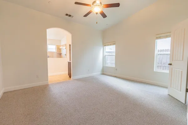 an empty room with chandelier fan and windows