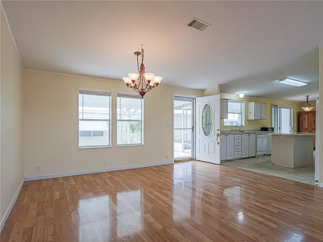 a view of an empty room and kitchen with wooden floor
