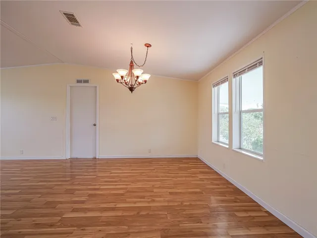 a view of an empty room with chandelier and wooden floor