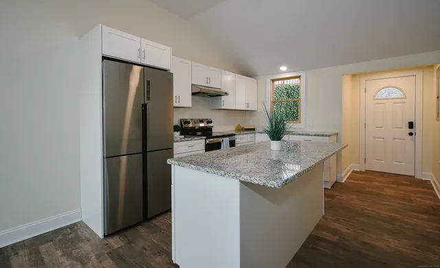 a kitchen with stainless steel appliances granite countertop a refrigerator a stove and a sink with wooden floor