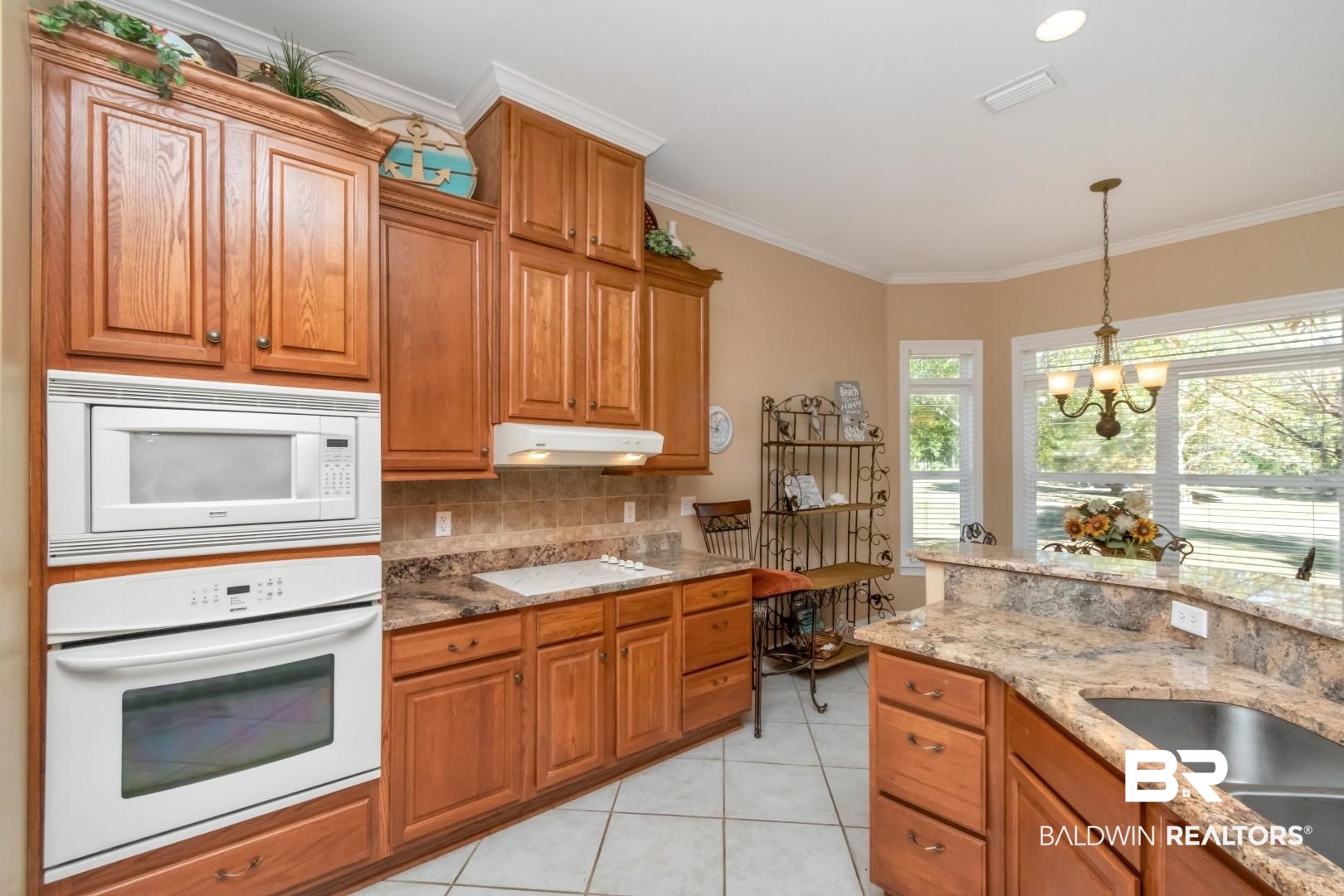 9905 Carnoustie Court Foley, AL 36535 - Photo 6 of 31 Kitchen featuring brown cabinetry, white appliances, light stone counters, crown molding, and backsplash