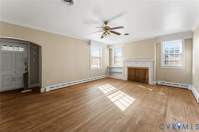 an empty room with wooden floor fireplace and windows
