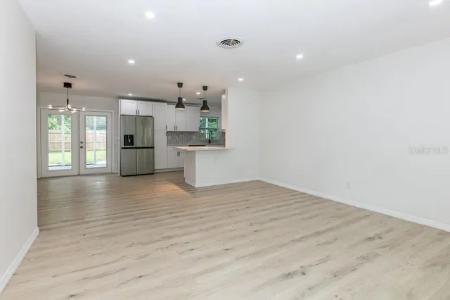 a view of an empty room and kitchen with wooden floor