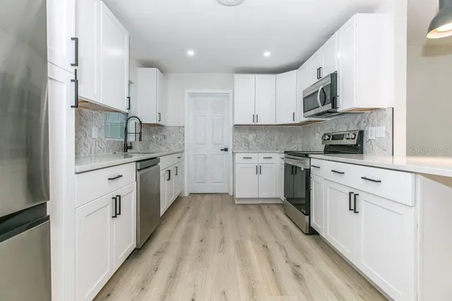 a kitchen with stainless steel appliances white cabinets a sink dishwasher a stove and a refrigerator with wooden floor