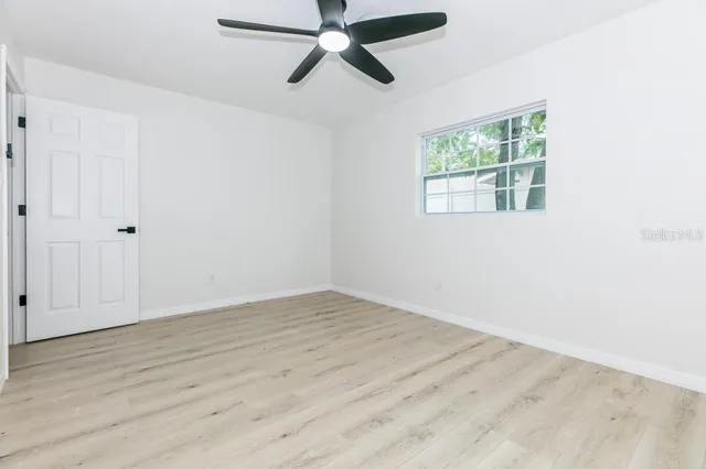 an empty room with wooden floor ceiling fan and windows