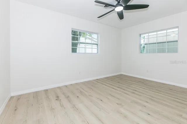 an empty room with wooden floor fan and windows