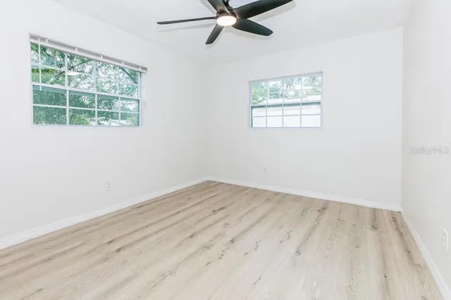 an empty room with wooden floor windows and fan