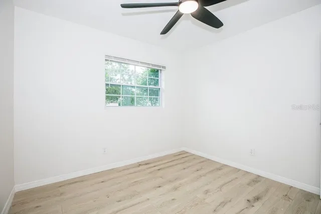 an empty room with wooden floor ceiling fan and windows