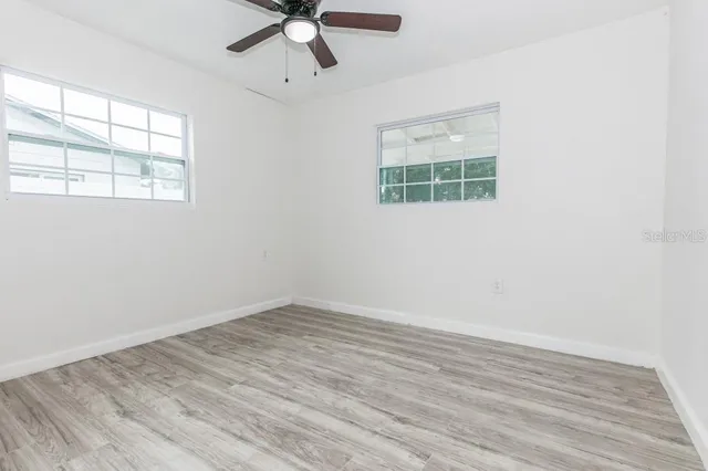 an empty room with wooden floor chandelier fan and windows