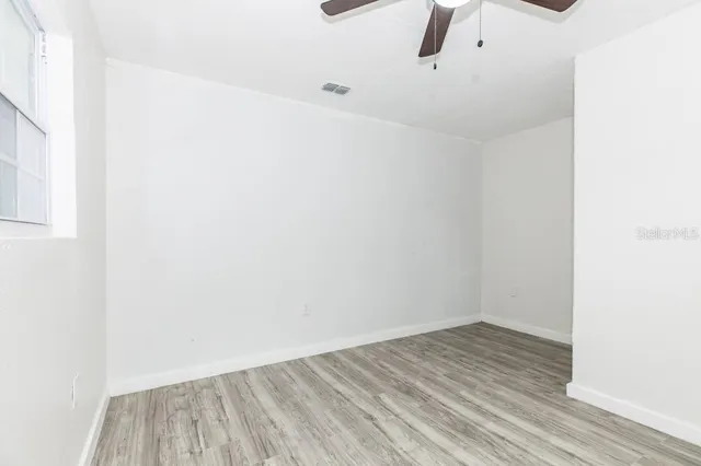 a view of an empty room with wooden floor and a ceiling fan