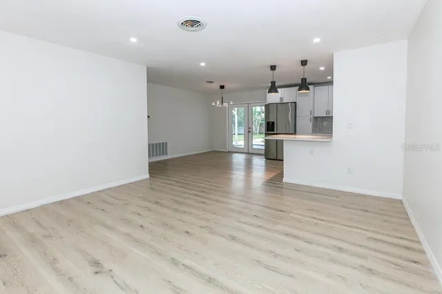 an empty room with wooden floor and kitchen view