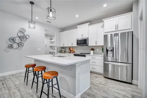 a kitchen with stainless steel appliances a refrigerator a sink dishwasher a stove and white cabinets with wooden floor
