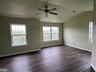 an empty room with wooden floor chandelier fan and windows