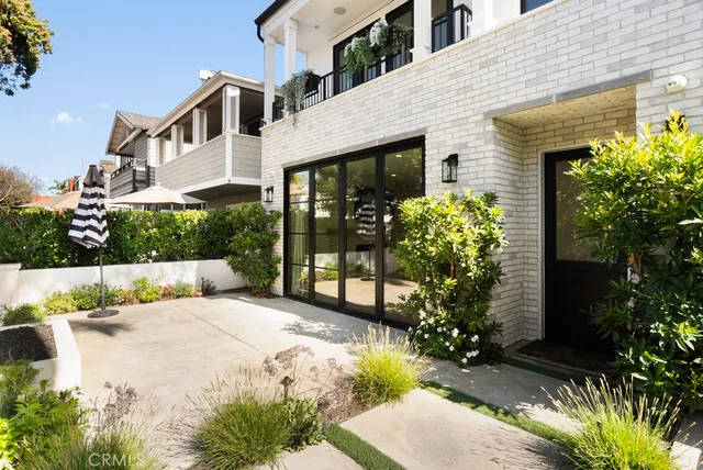 a view of a white house with large windows and flower plants