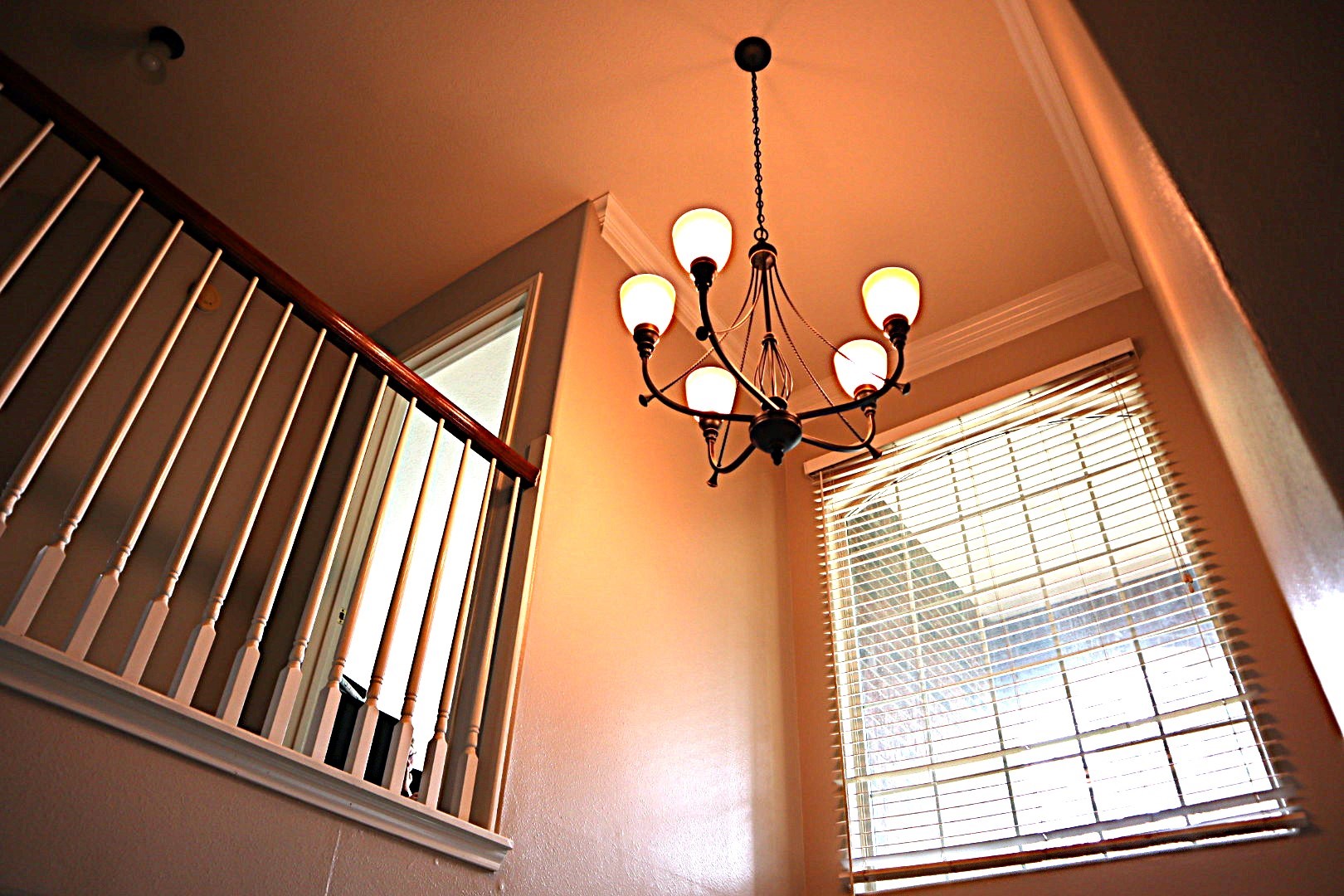 19114 Emory Trail Spring, TX 77388 - Photo 19 of 32 This view showcases a stairway landing with a stylish chandelier and a large window with blinds, offering ample natural light. The railing features classic white spindles with a wooden handrail, complementing the neutral wall tones.